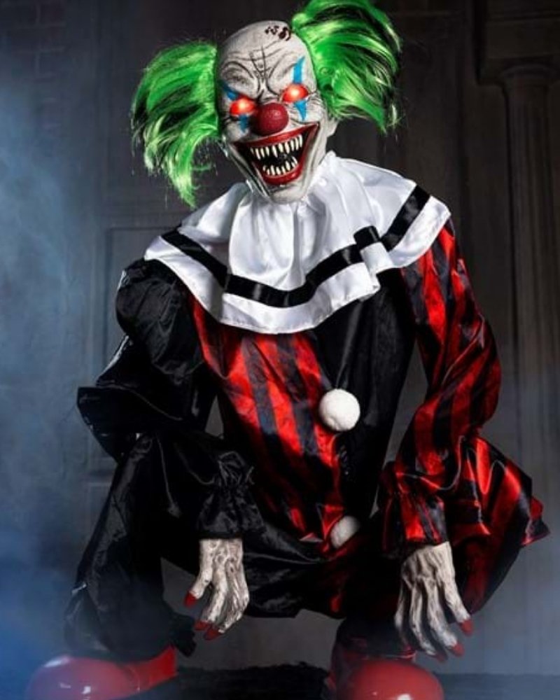 Crouching animatronic clown Halloween decoration with green hair and glowing eyes