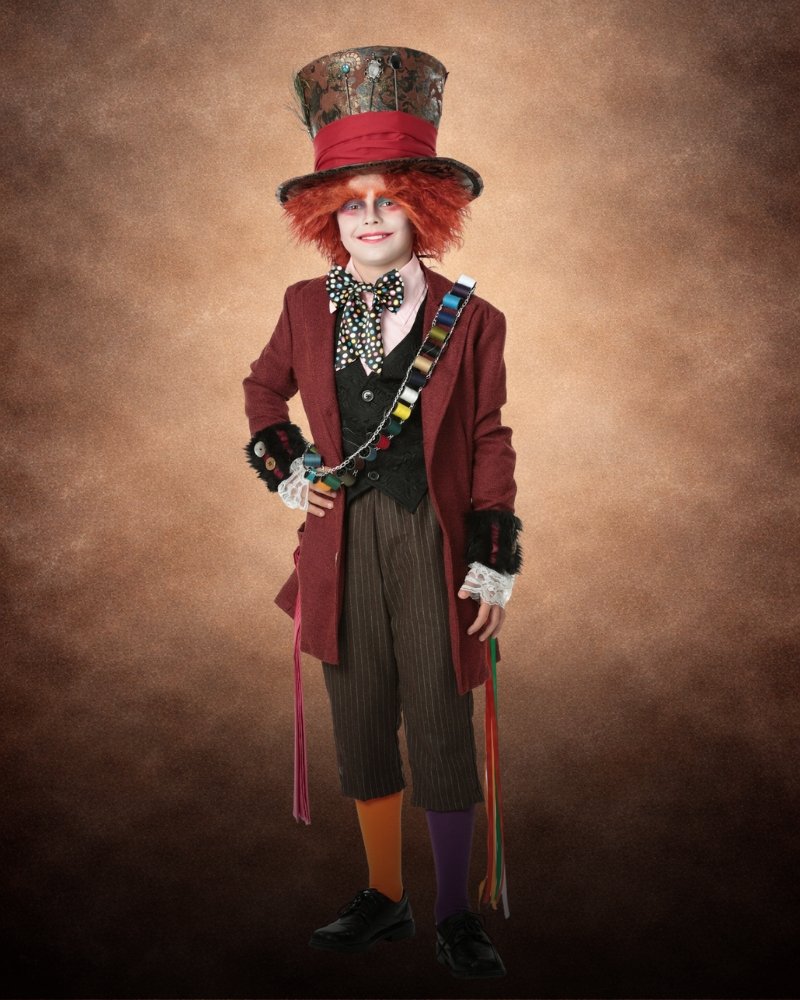 Authentic Mad Hatter costume for kids featuring a burgundy tailcoat, striped trousers, oversized top hat, colorful sash, polka dot bow tie, mismatched socks, and bright red hair.
